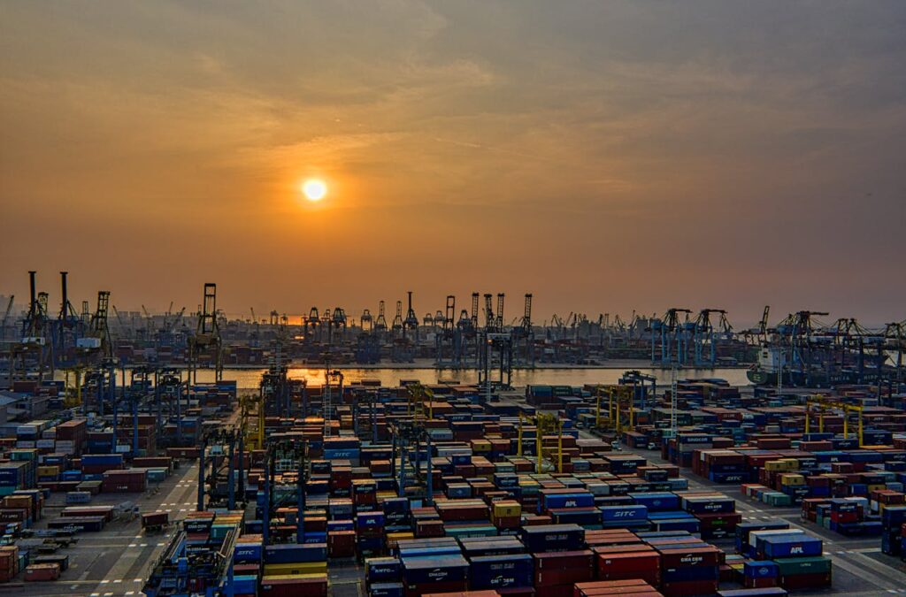 Sunset over a bustling seaport filled with stacked shipping containers and cranes.
