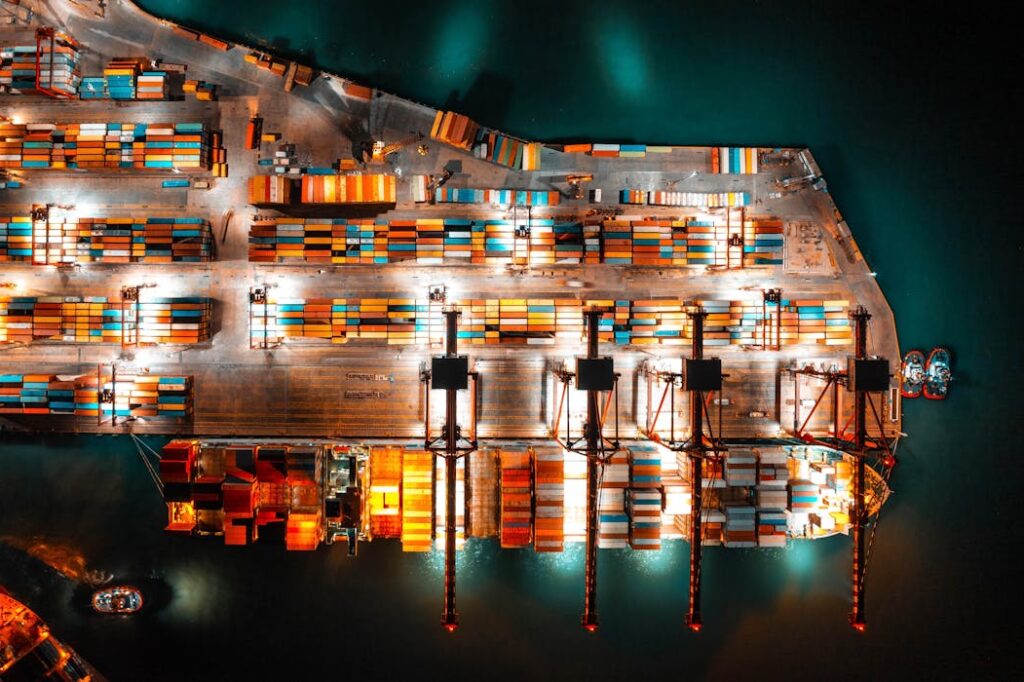 Dramatic aerial view of a busy shipping port with colorful containers and bright lights at night.
